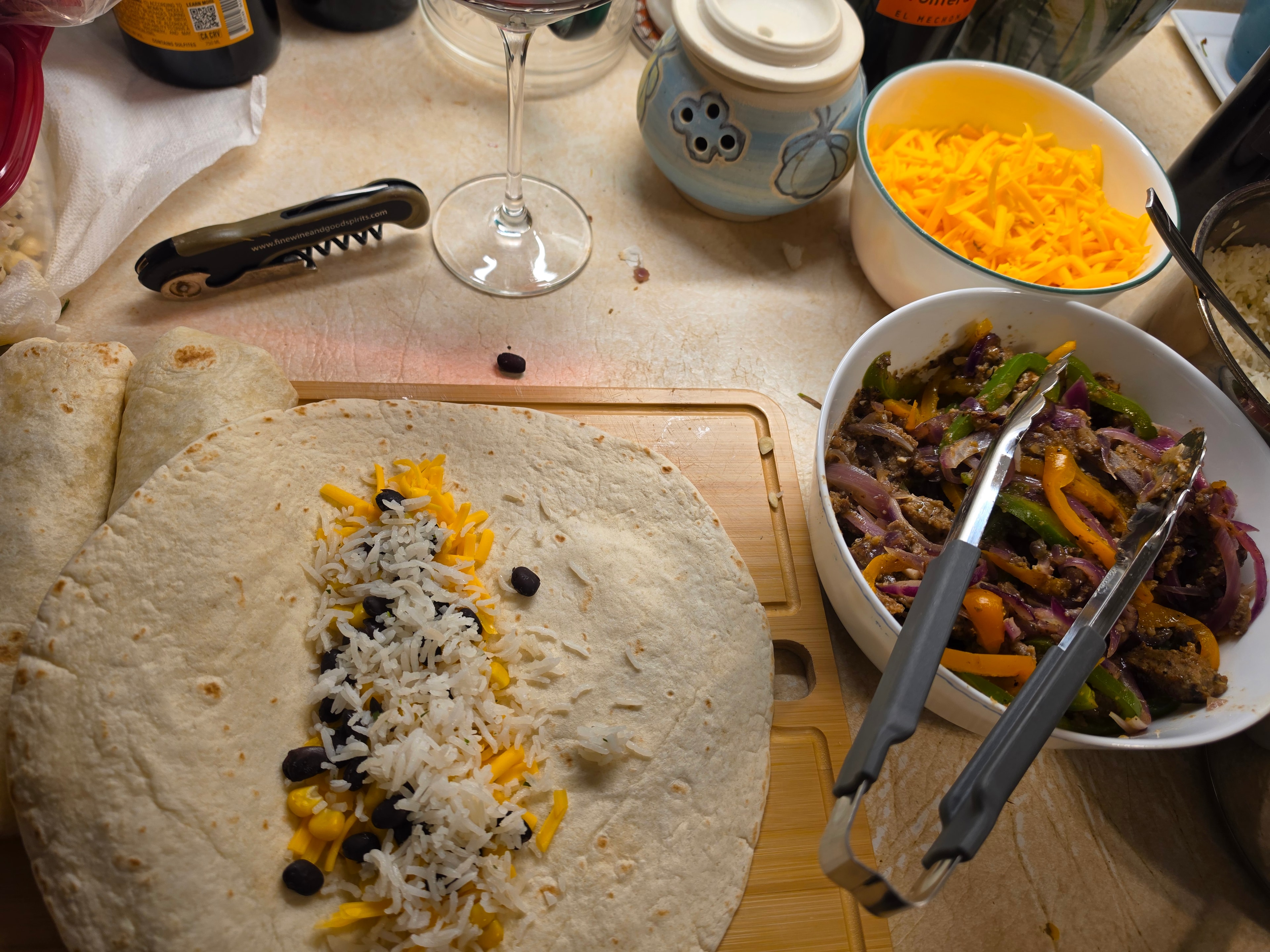 Burrito assembly with rice, black beans, cheese, and filling — wine glass in frame