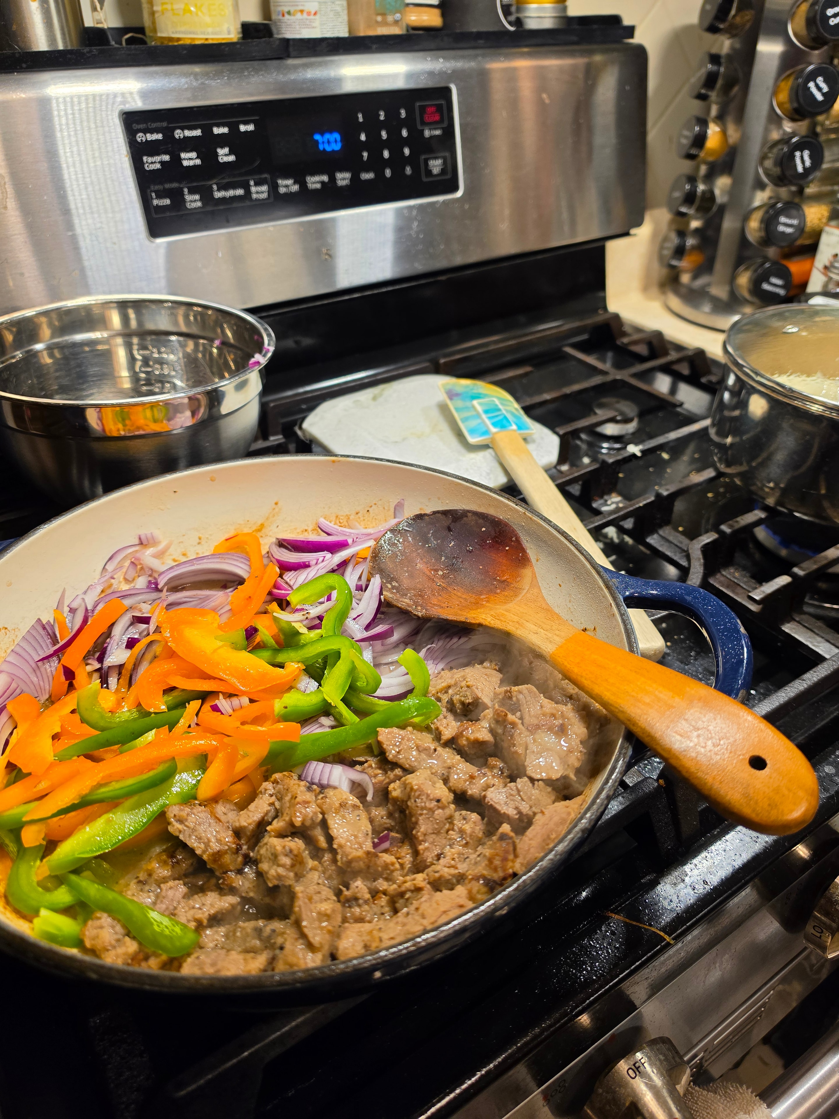 Steak, peppers, and onions cooking in a pan on a messy stove