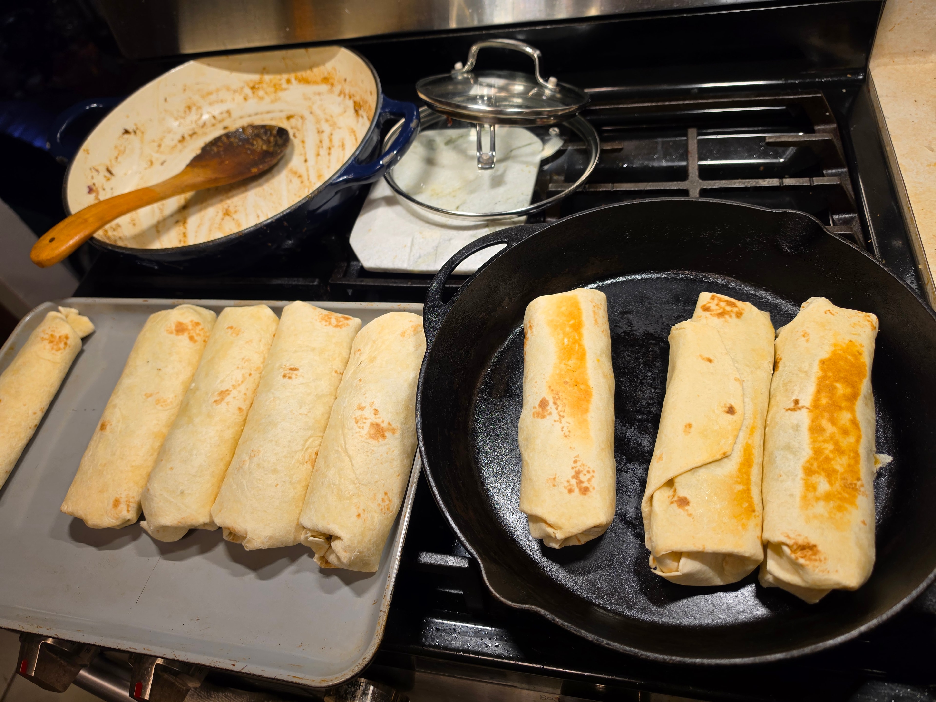 Batch of burritos sealing in cast iron skillet and on a tray
